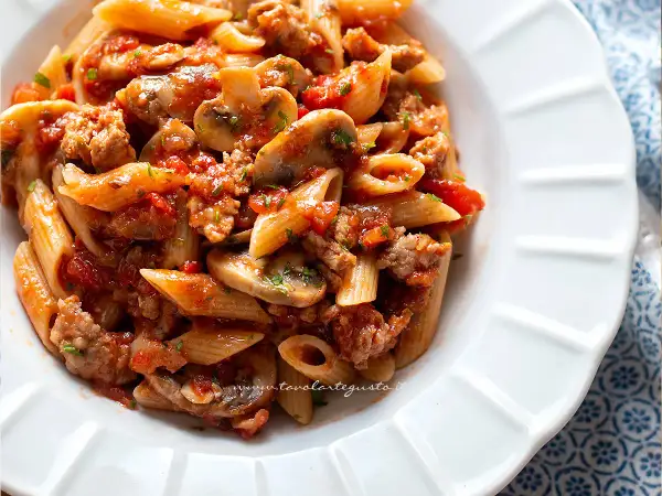 Piatto di pasta alla boscaiola con penne, funghi, salsiccia e pomodoro, un classico saporito.