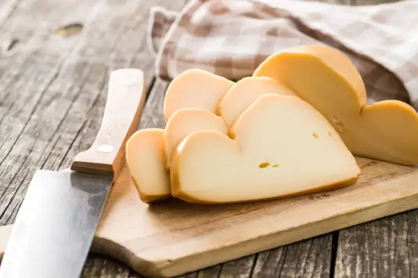 Tagli di **la provola** affumicata su un tagliere di legno, accanto a un coltello.