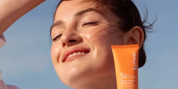 Une jeune femme rayonne sous le soleil, protégeant sa peau avec un fluide solaire. Un rappel : mettre de la crème solaire tous les jours pour une peau éclatante.