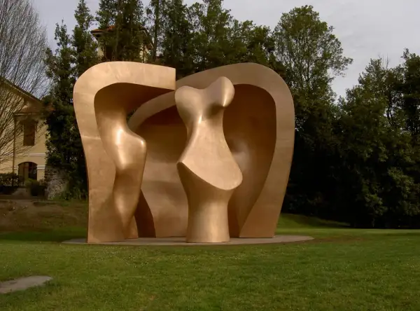 Escultura abstracta dorada en el parque de los pueblos de Europa, con formas curvas y orgánicas, rodeada de césped y árboles frondosos.