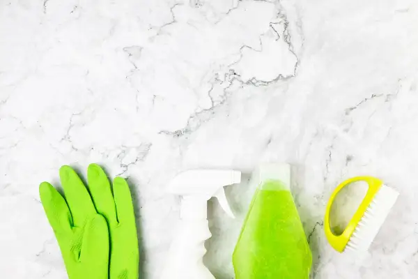 Guanti verdi, spray bianco, flacone di liquido verde e spazzola gialla pronti per scoprire come pulire pietra.