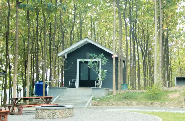 Mały, ciemny domek letniskowy w lesie, z kamiennym paleniskiem i ławką. Idealne miejsce na wypoczynek, z solidnymi bloczkami pod domek letniskowy.