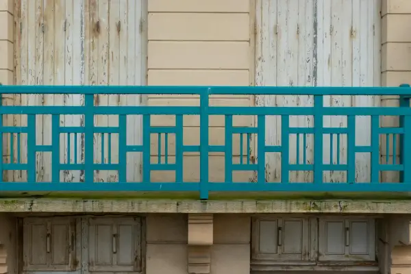 Turkusowe, geometryczne mocowanie balustrady od czoła, z widocznymi odrapanymi drzwiami poniżej.