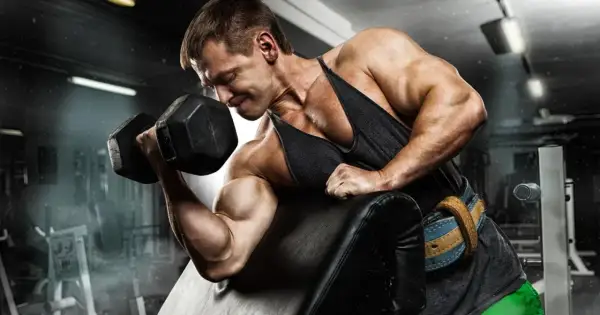 Kulturysta z determinacją ćwiczy biceps, napinając mięsień trójgłowy ramienia podczas podnoszenia ciężaru.