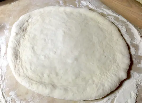 Pâte à pizza étalée sur une surface farinée, prête pour une recette pâte à pizza rapide.