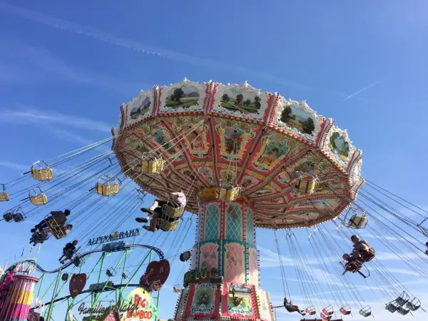 Carrusel giratorio en un oktoberfest parque de atracciones, con gente disfrutando del paseo bajo un cielo azul.