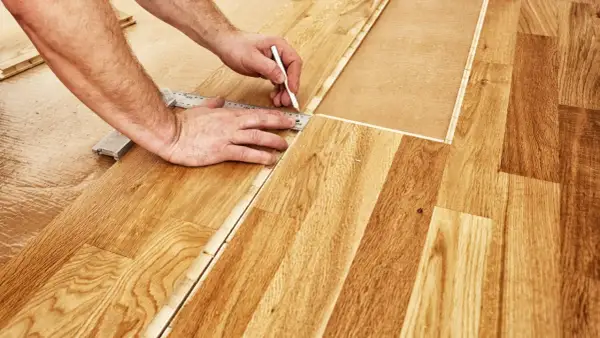 Un bricoleur utilise une règle et un crayon pour marquer une ligne de coupe sur du parquet flottant, étape essentielle pour savoir comment couper du parquet flottant.