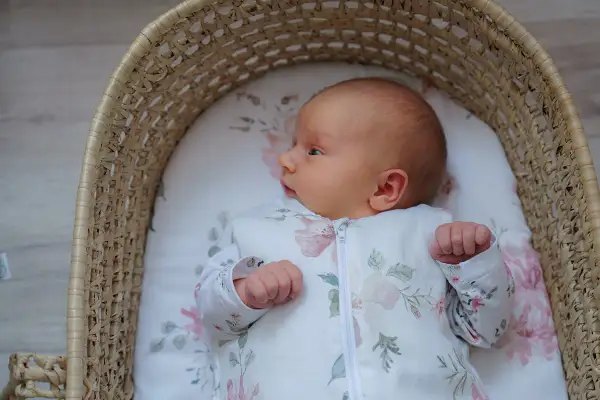 Malutkie dziecko w śpiworku z motywem kwiatowym, leżące w wiklinowym koszu. Od kiedy kołderka dla niemowlaka jest tak urocza?