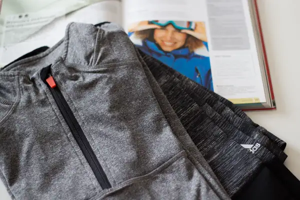 Szara bluza sportowa z zamkiem, obok otwarta książka z narciarką. Czy poliamid materiał czy oddycha?