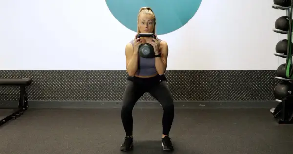 Woman performing kettlebell squat pulses in a gym.