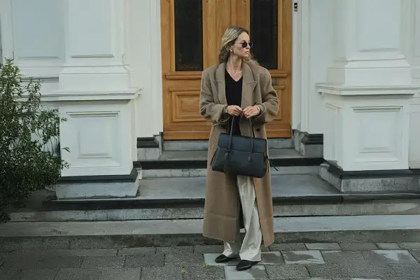En kvinna med solglasögon bär en elegant brun kappa och håller en stilren vero moda väska.