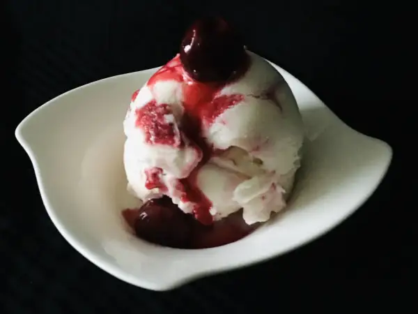 Ein Löffel cremiges Sauereis mit Kirschsauce und einer ganzen Kirsche obendrauf, serviert in einer weißen Schale.