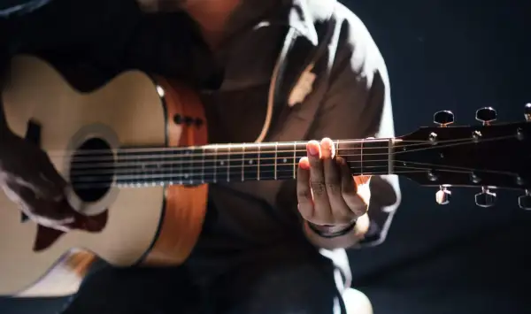 Person übt das Spielen einer akustik gitarre. Hände formen Akkorde auf dem Griffbrett, während die andere Hand die Saiten anschlägt.