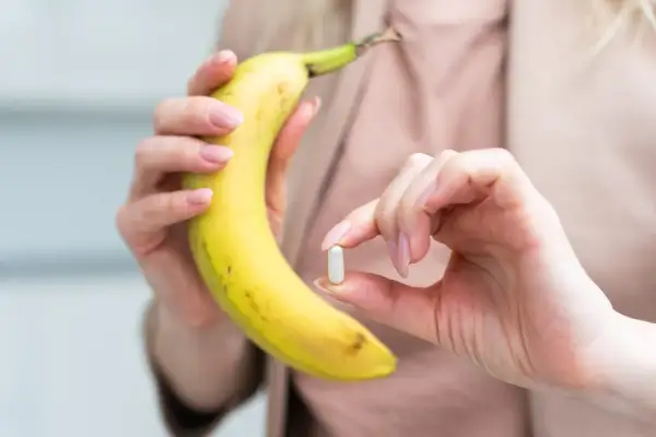 Dłoń trzymająca banana i kapsułkę, sugerującą potas najlepiej przyswajalny z natury i suplementów.