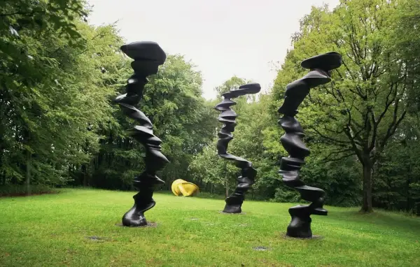 Drei schwarze, verdrehte Skulpturen stehen im **Skulpturenpark Wuppertal** auf einer grünen Wiese vor Bäumen. Eine gelbe Skulptur liegt im Hintergrund.