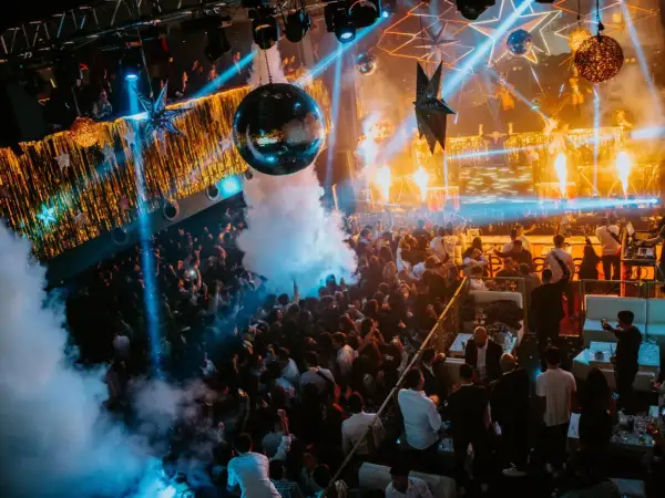 Multitud bailando en una discoteca con luces de neón, humo y una bola de discoteca, celebrando la nochevieja en Zaragoza.