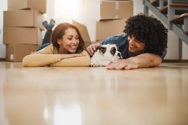 A happy couple and their bulldog relax on the floor amidst moving boxes, ready for their new home.