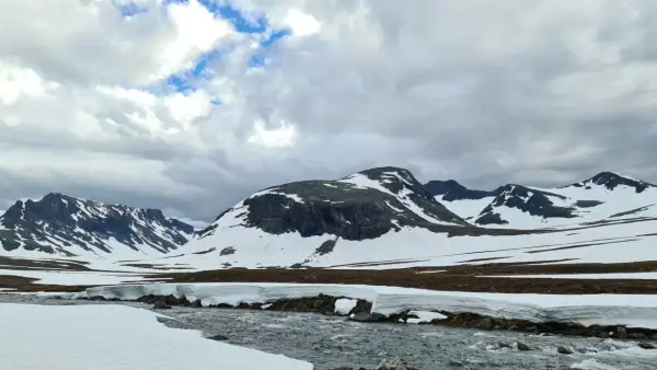 Snöklädda berg och en forsande älv i Jämtland, en vy som inspirerar till att bestiga Sylarna.