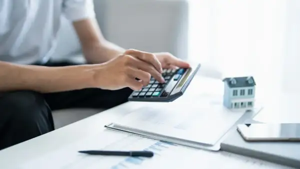 Man calculando la viabilidad hipoteca con calculadora, papeles y maqueta de casa.