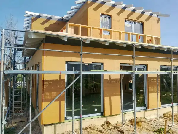 Casa en construcción con paredes exteriores prefabricadas de madera, andamios y cielo azul.
