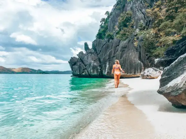 Frau genießt das türkisfarbene Wasser und den weißen Sandstrand auf den Philippinen. Ein perfekter Ort für Backpacking-Abenteuer.