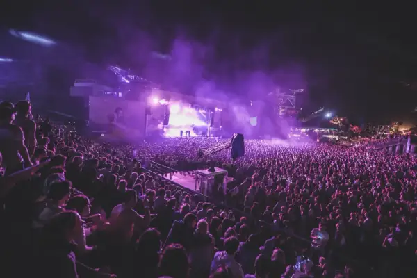 Tłum ludzi na nocnym koncercie, fioletowe światła i dym tworzą magiczną atmosferę. To niezapomniane u2 koncerty.