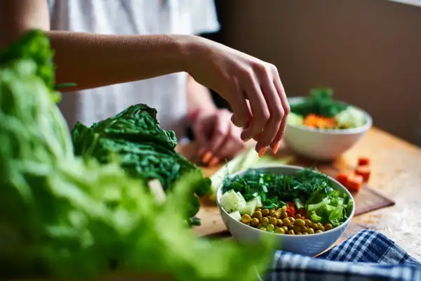 Mano che aggiunge erbe fresche a un'insalata colorata, ricca di fibre insolubili come piselli e verdure croccanti.