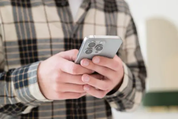 Osoba w kratę trzyma smartfon, szukając informacji, jak odzyskać usunięte wiadomości SMS.