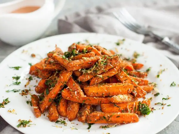 Karmelizowana marchewka, posypana ziołami i parmezanem, podana na białym talerzu.