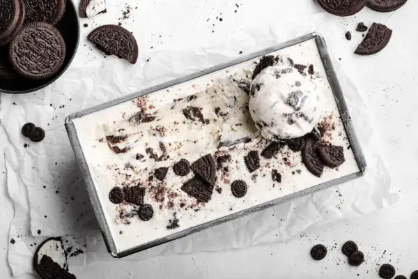 Selbstgemachtes Oreo Eis in einer Metallform, mit einem Löffel und zerbrochenen Keksen garniert. Perfekt für alle, die Oreo Eis selber machen wollen.