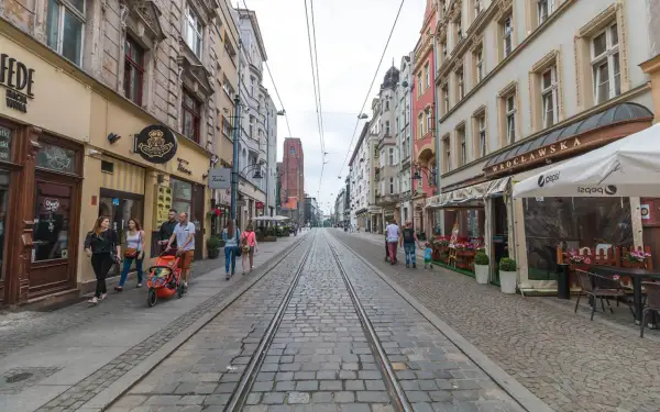 Spacer po starówce Wrocław, ulica z torami tramwajowymi i kamienicami. Rodzina z wózkiem spaceruje po bruku.