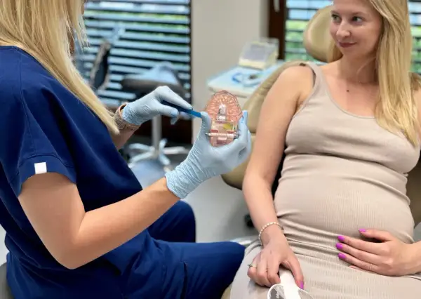 Dentystka pokazuje ciężarnej pacjentce model szczęki, omawiając higienę jamy ustnej. Piaskowanie zębów w ciąży jest bezpieczne i zalecane.