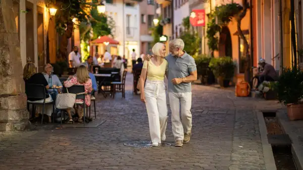 Ein älteres Paar spaziert abends durch eine Gasse in Freiburg. Was kann man in Freiburg machen? Hier: gemütlich essen gehen und die Atmosphäre genießen.