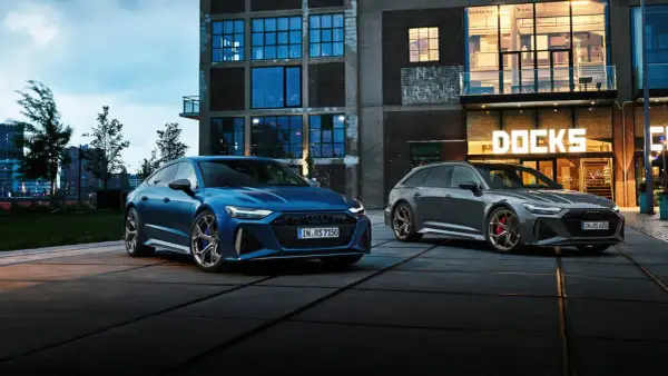 Dwa Audi RS6: niebieski sedan i szary Avant, zaparkowane przed budynkiem z napisem "DOCKS".