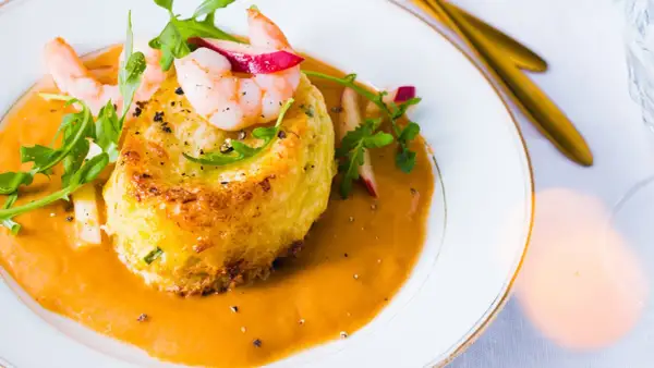Un délicieux soufflé de crabe, nappé d'une bisque onctueuse et garni de crevettes et de roquette.
