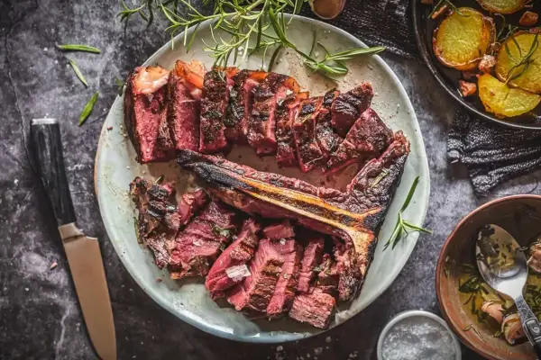 Aufgeschnittenes, perfekt gegrilltes Bistecca alla Fiorentina mit Rosmarin und Beilagen.