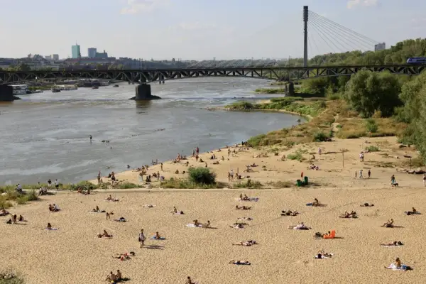 Słoneczna poniatówka nad Wisłą. Ludzie opalają się na piaszczystej plaży, w tle most i panorama Warszawy.