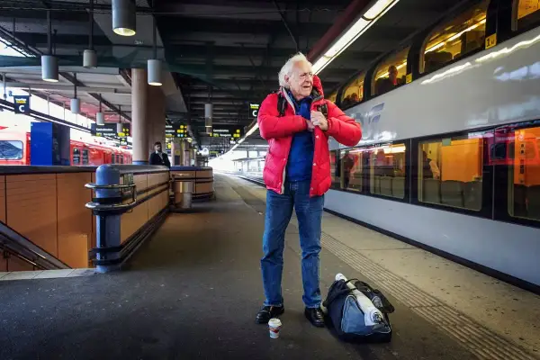 Äldre man i röd jacka på tågstationen, kanske på väg att resa som Kay Pollack.
