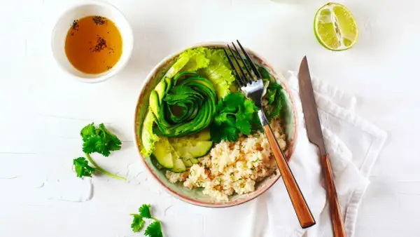 Un fresco e colorato cous cous freddo con avocado a spirale, cetrioli, lattuga e erbe aromatiche.
