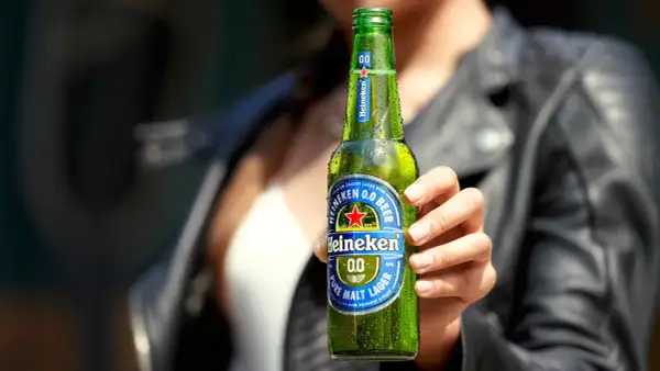 Mano che tiene una bottiglia di Heineken 0.0, la birra senza glutine, rinfrescante e gustosa.