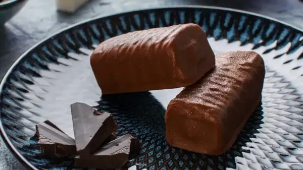 Dwa czekoladowe batony proteinowe na talerzu, obok kawałki gorzkiej czekolady. Idealne do domowego batony proteinowe przepis.