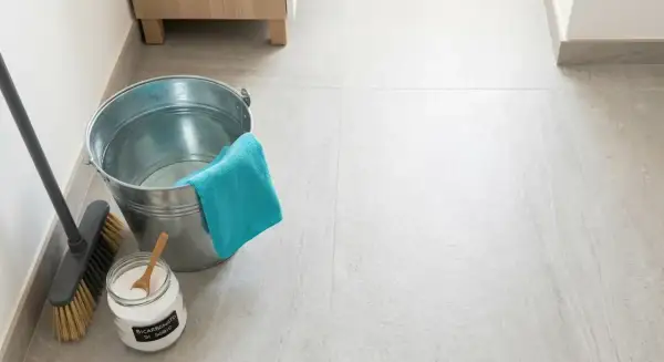 Secchio, scopa e barattolo di bicarbonato per pavimenti, pronti per una pulizia profonda.