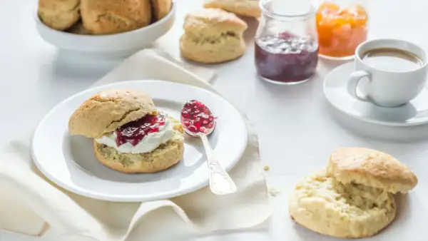 Ein Scone mit Clotted Cream und Marmelade, daneben eine Tasse Kaffee und weitere Scones.