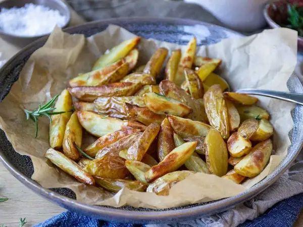 Krispiga klyftpotatis i airfryer, gyllene och redo att serveras med en kvist rosmarin.
