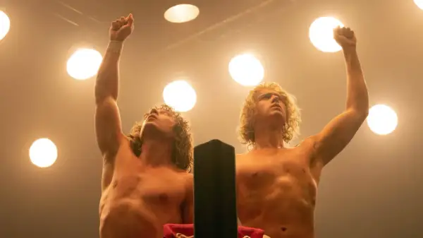 Zwei Wrestler mit blonden Locken, die unter Scheinwerfern die Fäuste gen Himmel strecken. Sie sind bereit, den "Iron Claw" zu zeigen.