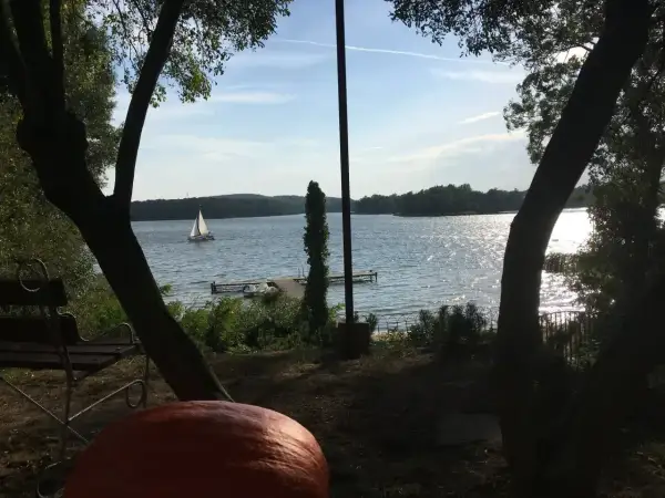 Sielankowy widok na jezioro w Sierakowskim Parku Krajobrazowym. Żaglówka sunie po falach, a na brzegu czeka ławka i dynia.