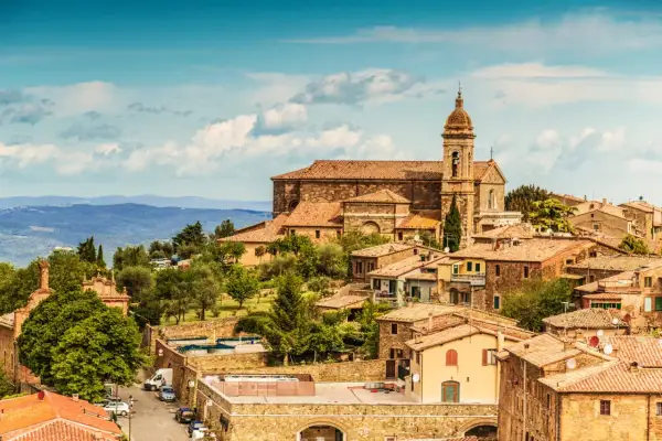 Panoramic view of Montalcino, Italy, with terracotta roofs, a church, and rolling hills under a blue sky.