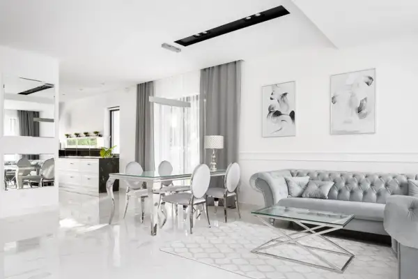 Eleganckie, nowoczesne wnętrze w stylu glamour. Błyszczące płytki, szara sofa i szklany stół tworzą luksusową atmosferę.