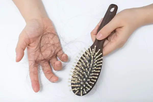 Une main tient une brosse à cheveux en bois, tandis que l'autre main montre une perte de cheveux. La lumière rouge met en évidence la perte de cheveux.