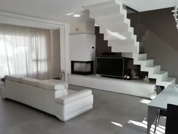 Soggiorno moderno con divano bianco, camino, TV e una scenografica scala a vista bianca. Ottime idee arredare soggiorno con scala a vista.
